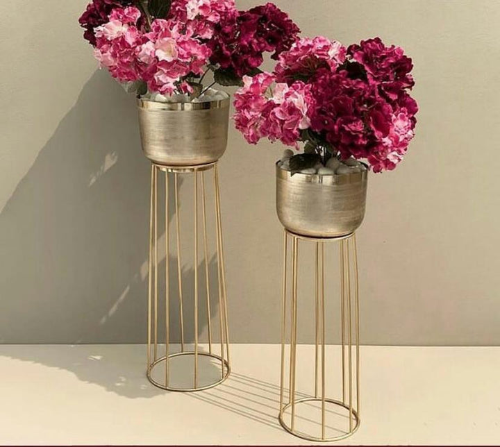 Two gold metal plant stands with pink flowers against a beige background